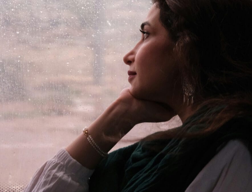 A female sitting at a window looking peaceful andcontemplative - "How to stop negative thoughts - person finding peace and calm"]